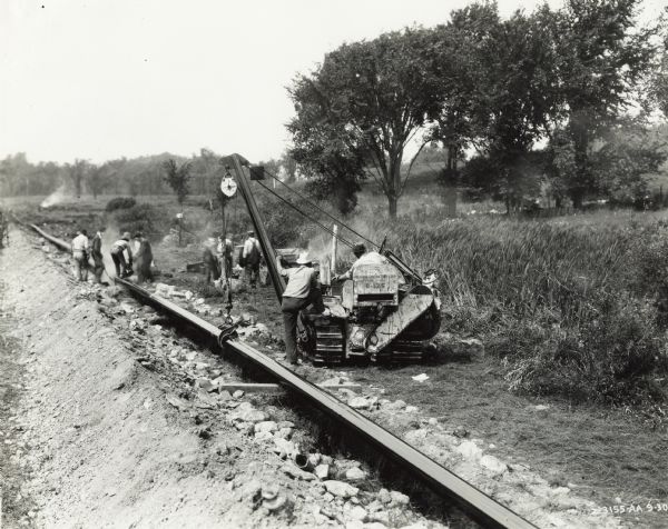 Workers lay a pipeline in a field using an International T-20 TracTracTor (crawler tractor) and sideboom. Original caption states: "Jones & Hannahan."
