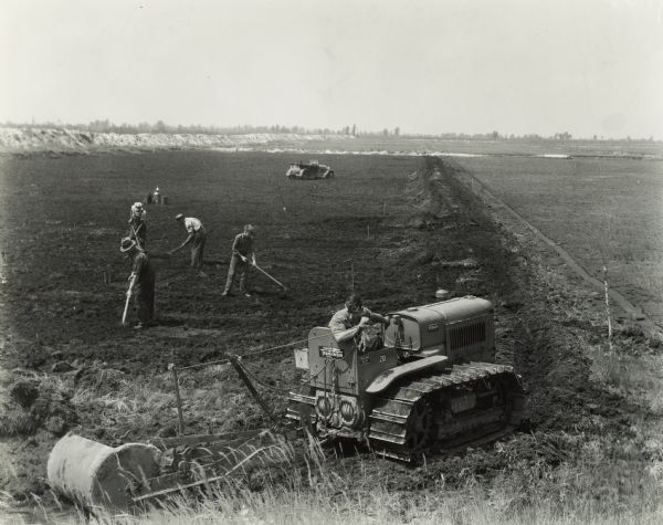 Men building a cranberry marsh using an International T-20 TracTracTor (crawler tractor) on the farm of Oscar O. Potter. The tractor is pulling a "turnover scraper". Original caption states: "Oscar Potter has 36 acres under production, his brother, Guy Potter, Camp Douglas, Wisconsin, has 65 acres.  Their father was also a cranberry raiser.  In his time, cranberries grew wild in this section, producing about 8 to 10 barrels to the acre.  The finest wild plants were selected, transplanted, again and again culled until the best varieties were obtained.  The old system was to plant them the same as other crops, paying no particular attention to the terrain of the soil.  Once planted they live forever if not frozen or baked out.  As better varieties have developed, old marshes have been destroyed and new plants set."