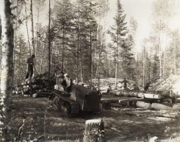 Men haul logs in a forest using an International T-20 TracTracTor (crawler tractor). Original caption states: "Owner, Frank Knaeble, working five miles south of Bena. 520 acres in this piece, basswood, poplar, and pine, producing 16,000 to 18,000 feet a day, 10 hours. Using 28 to 32 gallons fuel, 2 quarts oil a day as compared to 50 gallons of gas, 2 gallons cylinder oil in old Case motor previously used. In 618 hours produced 960,000 feet of lumber. You could not give him any other kind of motor for his mill."