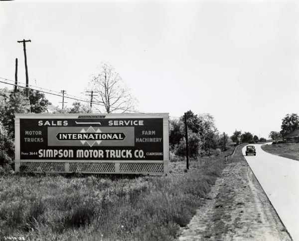 An automobile drives down a road near a billboard advertising the Simpson Motor Truck Company, an International truck dealership. The original caption reads: "The Simpson Motor Truck Company, Clarksburg, West Virginia, very effectively advertises its business by means of three big conspicuously placed painted signs on important highways near the city. Each is 12 by 40 feet in size and is painted in six colors.  It costs $60 a month rental for these signs."