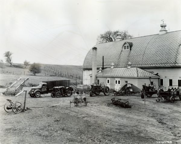 Equipment owned by the Pine Tree Stock Farm is displayed outside a barn. The original caption describes the equipment shown as a "D-30 M.T. [motor truck], W-30 tractor and #8 Little Genius plow, 7-20 and #22 1-G cultivator, F-20 and #10 mower, corn planter, #7 mower, #10 cultipacker, #4 spreader, and a hay loader."