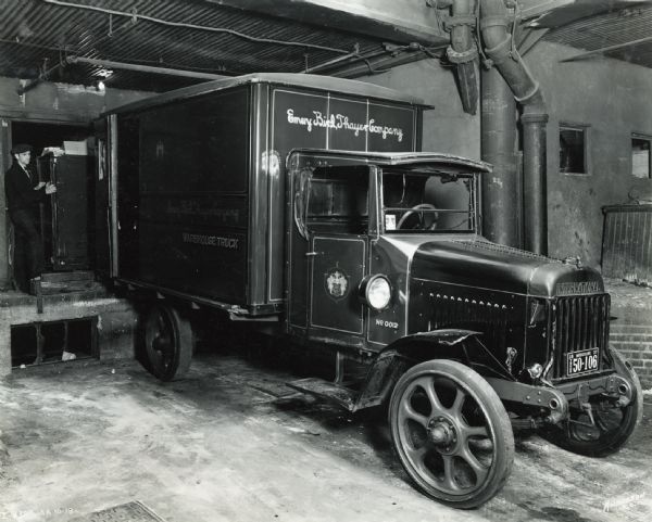 International delivery truck used by the Emery Bird Thayer Dry Goods Company. A man is standing behind the truck on a loading dock.