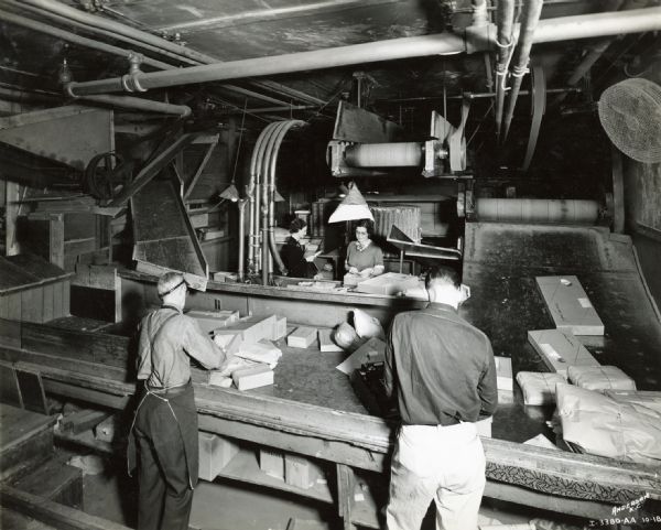 Men sorting packages in the shipping department of the Emery, Bird, Thayer Dry Goods Company as women credit clerks work in the background.