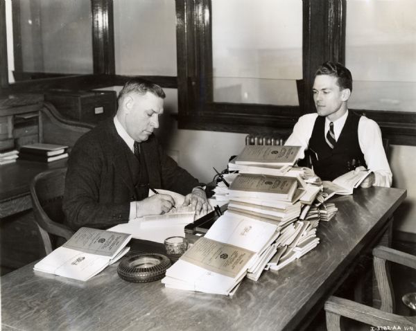 Branch manager A.L. Weller goes over 1938 dealer contracts at a desk, with another man seated by his side.