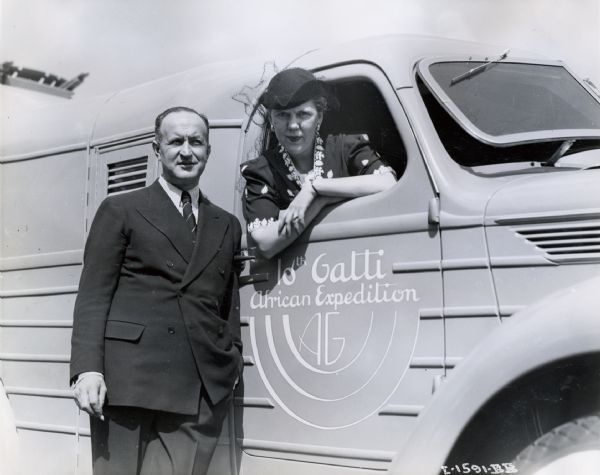 Mrs. Ellen Waddill Gatti leans from the window of a truck marked "10th Gatti African Expedition," while Commander Attilio Gatti stands outside the vehicle beside her. The truck was also known in company promotional literature as a "jungle yacht."