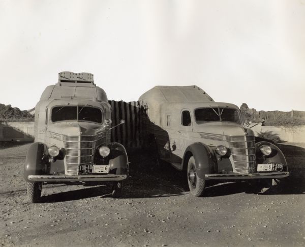 Two specially designed International trucks connected with an awning at an African camp site. The camp site was home to an Attilio Gatti expedition. The specially designed trucks were referred to in company advertising as "jungle yachts." The original caption reads: "Showing covered awning walkway making complete five-room apartment of the Gatti trailers on camp location in Africa.  One trailer has living and dining room, library, bar and electric kitchen.  The other has two ultra-modern bedrooms and tile bath with full-length tub in color harmony."