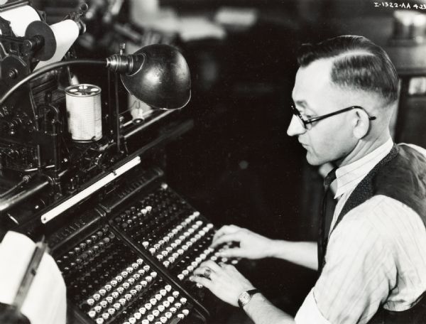 Man typing on a monotype keyboard, possibly in a Harvester Press production area.