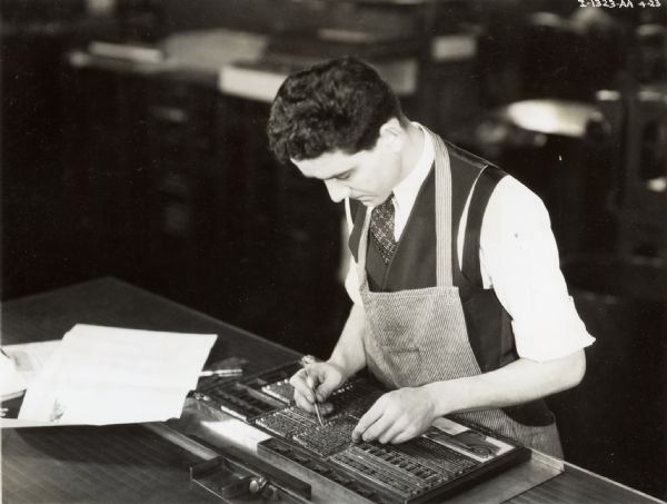 Man in an apron, composing metal type to be printed. The man may have been a worker at the Harvester Press.