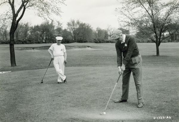International Harvester executives on a golf course. J.L. McCaffrey, director of sales, lines up a putt as H.N. Ross, district manager of the central district, watches from the background. J.L. McCaffrey later became president of the company.