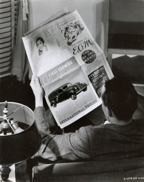 A man in an armchair reads a newspaper featuring an advertisement for International trucks.