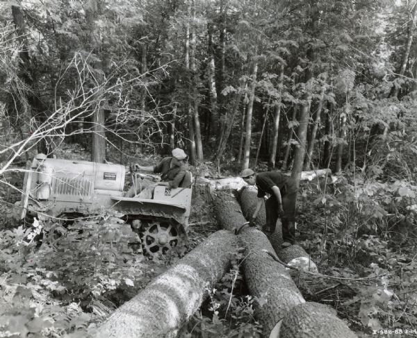 Two men use an International T-20 TracTracTor (crawler tractor) to log in a forest.