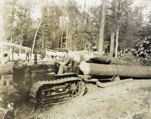 A man uses an International T-20 TracTracTor (crawler tractor) and PD-40 owned by Andrew Hedstrom to log, saw, and finish work on the Gun Flint Trail. The original caption reads: "T-20 and PD-40 owned by Andrew Hedstrom, Grand Marais, Minnesota.  Logging, sawing, and finishing 6 miles north on the Gun Flint Trail.  Produced 10,000 feet on August 19, 1937.  Tractor used to haul in logs.  Other power used on sawmill.  PD-40 used on planer and mill work, using 6 gallons of fuel in 8 hours.  Hedstrom and his sons own this industry, all working together and thoroughly sold on McCormick-Deering power.  Stated the tractor is getting bigger every day.  Was skeptical at first and did not believe it was powerful enough to do the work but now is an enthusiastic booster."