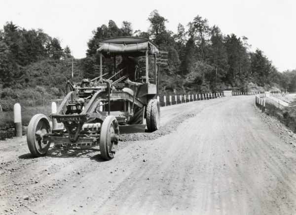 Emil Anderson operates a road grader marked "Russell Motor Patrol No.3" on Highway 12.