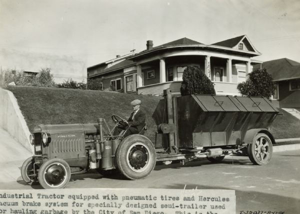 A man uses a McCormick-Deering 10-20 industrial tractor equipped with pneumatic tires and Hercules vacuum brake system to pull a specially designed semi-trailer used for garbage hauling. The tractor is in a residential neighborhood and there is a house in the background. The original caption reads: "This is the first of a number of similar units to be delivered for this work. Claimed this unit picks up load in one hour less time and at considerable less operating expense."