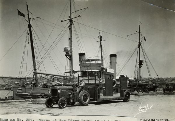 A man pulls a "reliance" semi-trailer with a McCormick-Deering 10-20 tractor near a docked ship in San Diego.