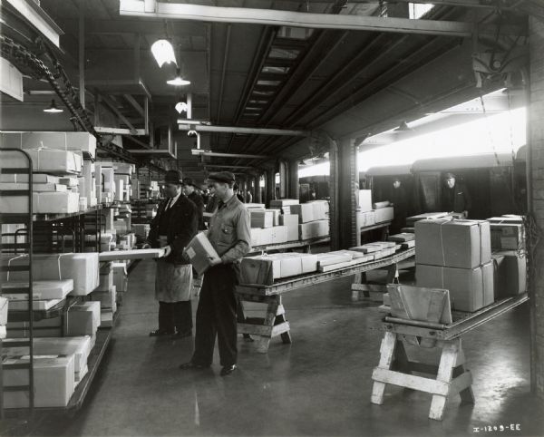 Men unloading trucks at the Railway Express Agency terminal at 11th Avenue and 42nd Street. The original caption reads: "Railway Express Agency terminal at 11th Avenue and 42nd Street, New York, showing trucks being unloaded, packages pushed along roller conveyors to men who sort them and place them on the proper track mounted conveyors in the center of the terminal."