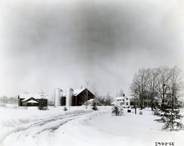 Several barns and a farmhouse surrounded by snow seen from across a road.