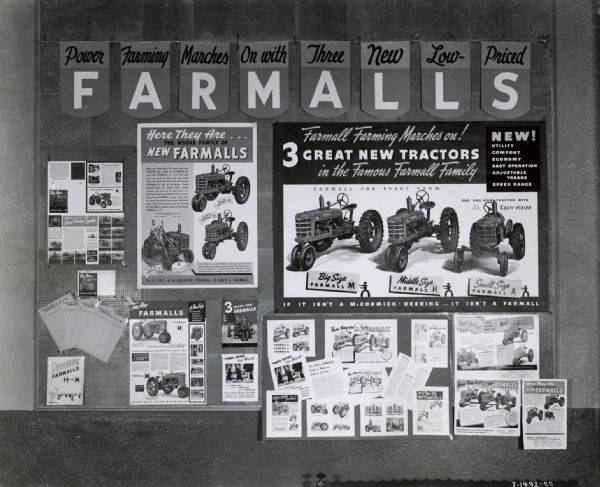 Bulletin board displaying a series of Farmall tractor advertising materials. The heading on the bulletin board reads: "Power Farming Marches On with Three New Low-Priced Farmalls." The board includes posters with the text: "Here they are . . . the whole family of new Farmalls" and "Farmall farming marches on!"