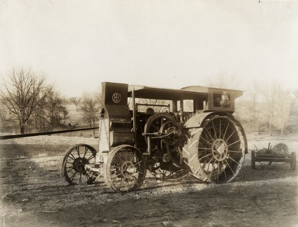A man is operating a Mogul 15-30 tractor with a belt attached to its power take-off. A cart is parked behind the tractor, and is carrying a barrel labeled: "White Rose Gasoline." Original caption states: "Mogul operating McC. Improved 6-Roll Husker and Shredder. Owned by W.L. Lehenbauer."