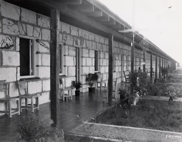 An exterior view of the housing for workers on an International Harvester sisal plantation in Cuba. A man is sitting on the porch in the distance. Caption on photograph reads: "A close-up view of new homes for the workers."
