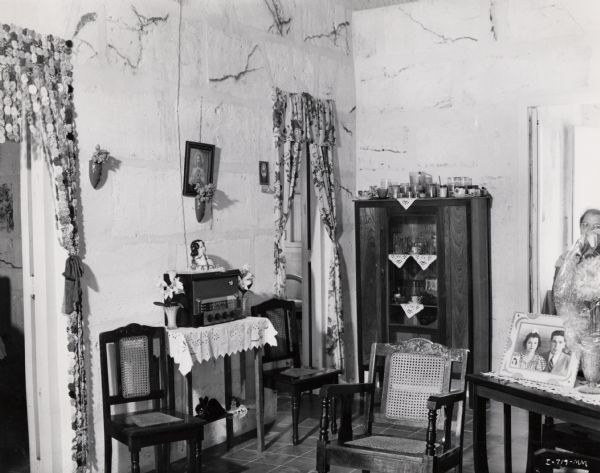 Chairs, photographs, a radio and other items in a workers' housing unit on an International Harvester sisal plantation in Cuba. Original caption reads: "Interior view of a native home."