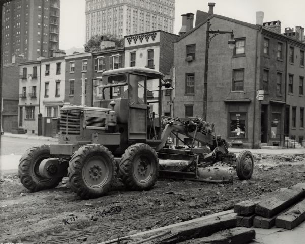 Men using a Number 3/2 Adams Motor Grader for road construction on Pine Street in Philadelphia. A laundry store is on the corner.