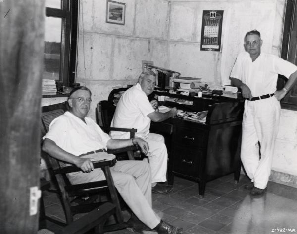Three managers in an office on an International Harvester sisal plantation in Cuba. Original caption reads: "Reading from left to right-Mr. Karn, Mr. Heath, and Mr. Monroe in the office at the plantation."