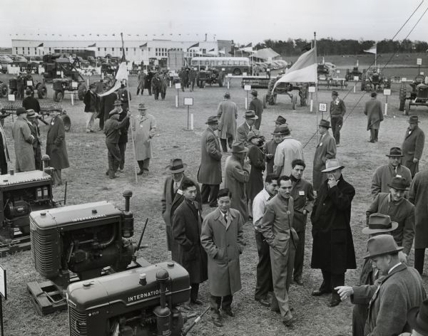 Groups of men examine International equipment on display outdoors at International Harvester's Hinsdale experimental farm. The equipment on display includes tractors and power units.