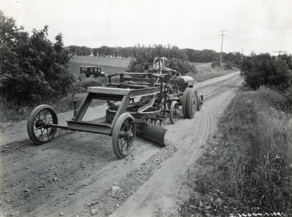 A man uses a McCormick-Deering 10-20 industrial tractor with a Stockland Whippet grader attachment to smooth a rural road.