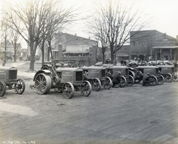 Men readying a line of McCormick-Deering 10-20 tractors for delivery for "tri-state tornado" victims. The tractors are parked in a row near what appears to be a park, and a line of storefronts are behind them.