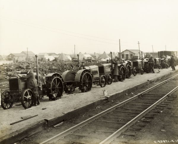 Men preparing newly arrived and unloaded McCormick-Deering relief tractors near railroad tracks. The tractors appear to be 10-20s.