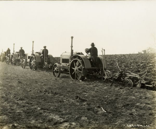 Relief directors drive McCormick-Deering 10-20 tractors to plow a field.