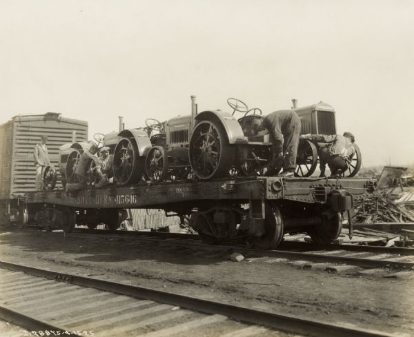 Men working on relief tractors on a flatbed railroad car for delivery to "tri-state tornado" victims.