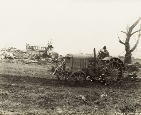 A man sitting on a McCormick-Deering tractor in a field.  Buildings damaged by the "tri-state tornado" are in the background. The tractor appears to be a 10-20.