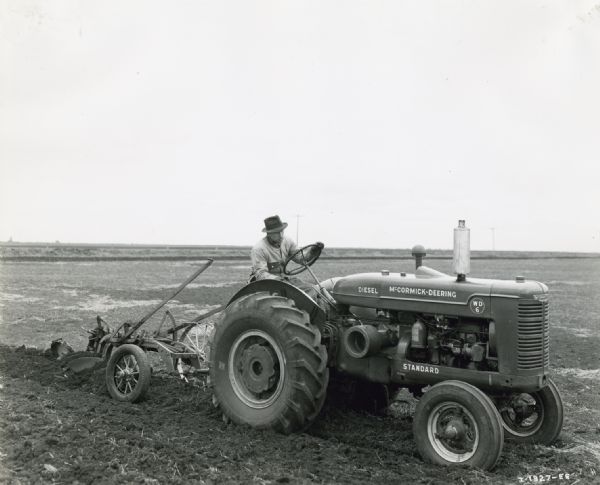 A man uses a McCormick-Deering WD-6 diesel tractor with a three bottom Little Genius plow to work in a field.