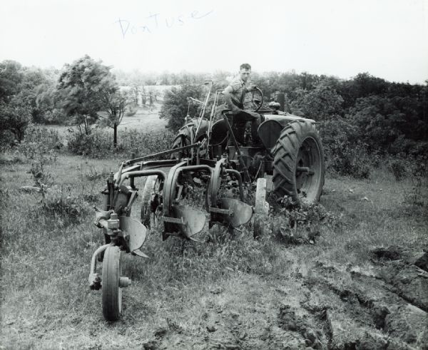 Paul F. Klassy uses a Farmall M tractor with a Number 15 Genius tractor plow to work in a field.