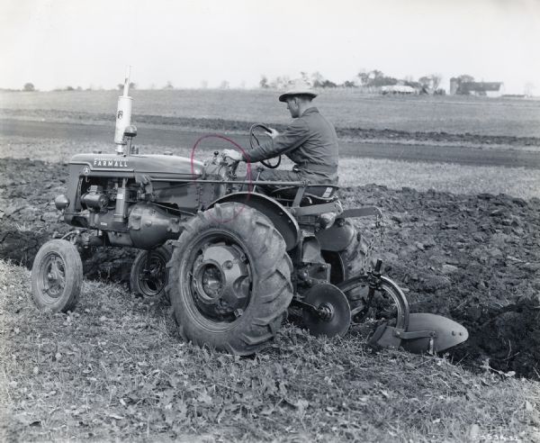 A man uses a McCormick-Deering Farmall A tractor equipped with two cylinder preproduction Touch-Control and single-bottom preproduction direct-connected plow [experimental].