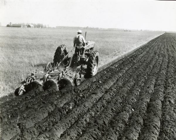 Rear view of Ed Stanley using a Farmall M tractor with a three bottom Genius plow on the Grassurere Land Company's home farm.