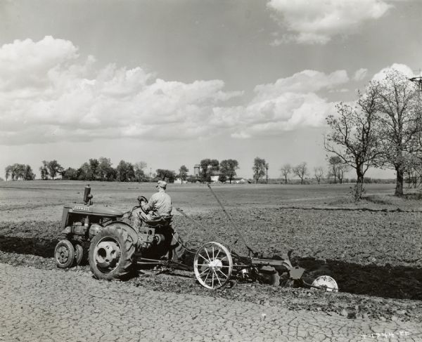 Side view from left of W.F. Rieschick, on his farm, using his McCormick-Deering Farmall M tractor.