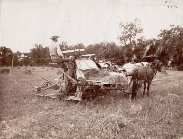 Man operating a McCormick wire binder driven by two horses through a field.