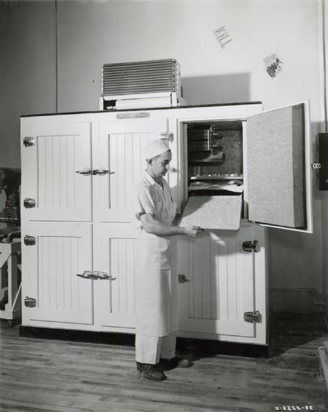 A male worker wearing a hat and apron at Johnson's Bakery removING a pan from an International reach-in cooler.