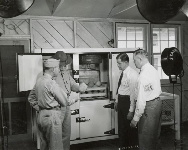 Men standING near an International condensing unit as it is being installed at Camp George G. Meade. The men appear to be examining a melon.