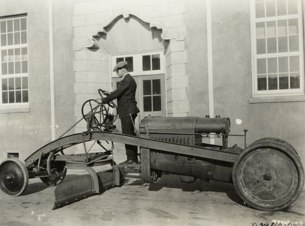 A man is standing on a Hadfield Penfield one-man grader outside the entrance to a building.