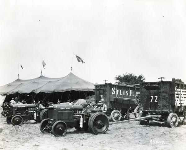 Men attach Sells Floto circus wagons to McCormick-Deering 10-20 industrial tractors in front of a circus tent.