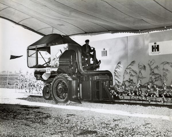 A man demonstrates a McCormick-Deering cotton picker under a tent on the Hinsdale experimental farm.