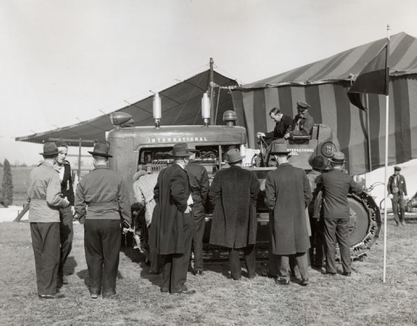 A group of men examine an International TD-24 crawler (TracTracTor) near a tent at International Harvester's Hinsdale experimental farm.