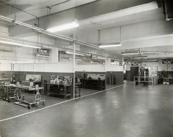 Interior view of International Harvester's Education and Training Center.  The large room appears to be divided into educational stations dedicated to different machinery parts and tools. Some of the stations are labeled: "Engines", "Carburator Electrical", "Diesel Injection", "Tools" and "Sheet Metal Printing".
