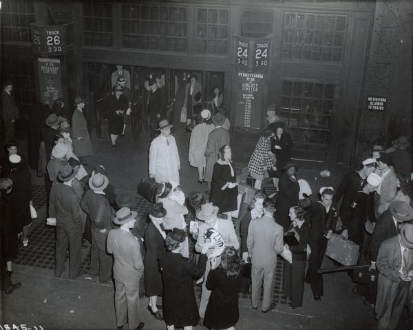 Elevated view of group of men and women gathered in a train station to greet passengers disembarking a train in a staged photograph for International Harvester's Education and Training Center.