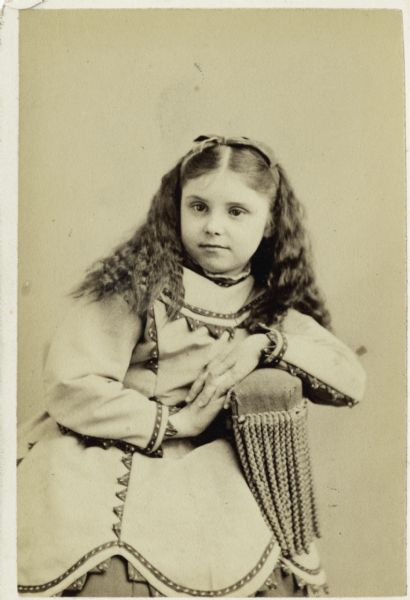 Studio portrait of Mary Virginia McCormick (1861-1941) as a girl, seated and leaning on the arm of a chair. She is wearing a decorated jacket and a ribbon in her hair.