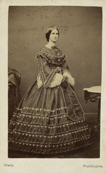 Carte-de-visite of Nettie Fowler McCormick (1835-1923) stands for a studio portrait wearing a floor-length dress.
